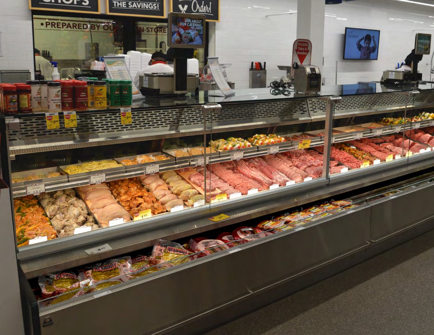 A well-stocked deli counter featuring a variety of meats, illuminated by a Lighting Solution Provider, with a service staff member in the background.